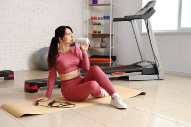 Spor salonunda ip atlayan, su içen genç bir kadın.