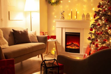 İçinde şömine, gri kanepe ve Noel ağacı olan şenlikli bir oturma odası.