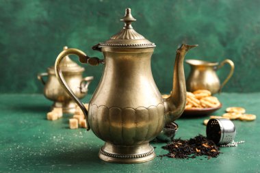 Yeşil masa üzerinde çay yaprakları olan klasik pirinç çaydanlık, yakın plan.