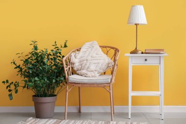 Sarı duvarın yanında lamba ve koltuk olan sehpa.