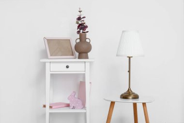 Tuvalet masasında okaliptüs dalları ve beyaz duvarın yanında lamba olan vazo.