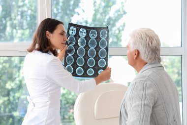 Kadın doktor muayenehanedeki yaşlı hastaya röntgen taraması gösteriyor.
