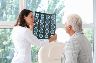 Female doctor showing x-ray scan to senior patient in medical office clipart