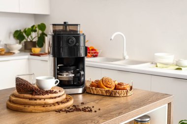 Mutfaktaki kahve makinesinde kavrulmuş fasulye, kahve fincanı ve çörekler.