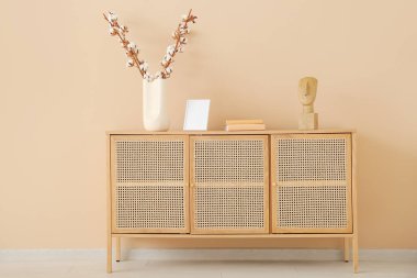 Pamuk dallı vazo, dekorasyon ve boş çerçeve bej duvarın yanındaki ahşap büfede.