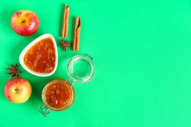 Kavanoz ve bir kase elma reçeli ve yeşil arka planda tarçın.