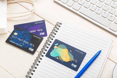 Beyaz ahşap arka planda kredi kartları ve bilgisayar klavyeli defter, yakın plan. İnternetten alışveriş