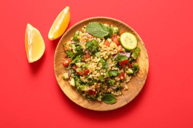 Lezzetli tabakta salata ve kırmızı arka planda limon parçaları.