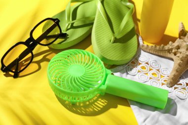 Sarı arka planda taşınabilir elektrikli yelpaze ve plaj aksesuarları olan kompozisyon, yakın plan.