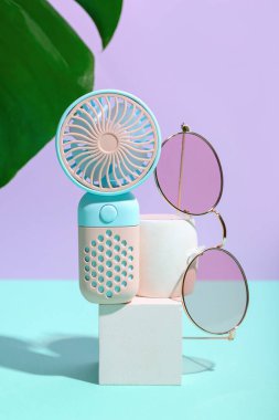 Taşınabilir elektrikli vantilatör, canavar yaprağı ve renkli gözlüklü sıva podyum, yakın plan.