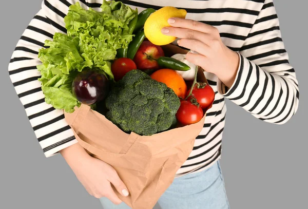 Woman holding paper bag with vegetables and fruits on grey background