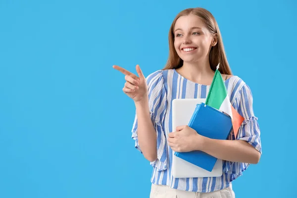 Young female student with flag of Italy and books pointing at something on light blue background