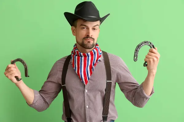 Handsome cowboy with horseshoes on green background