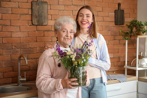 Young woman with her grandmother and flowers in kitchen