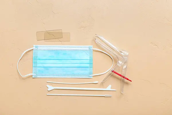 Gynecological speculum, medical mask and pap smear test tools on beige background