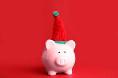 Kırmızı arka planda Noel şapkalı domuz kumbarası