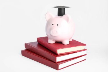 Mezuniyet şapkası ve beyaz arka plan kitapları olan domuz kumbarası.