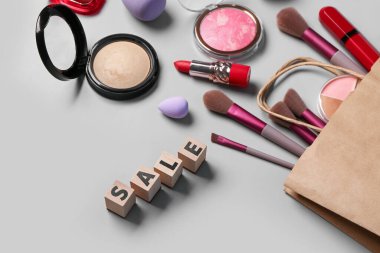 Makyaj malzemeli alışveriş çantası ve gri arka planda metin satışı, yakın plan.