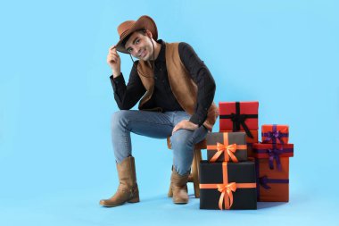 Cadılar Bayramı için giyinmiş genç adam mavi arka planda oturan hediyeli kovboy.