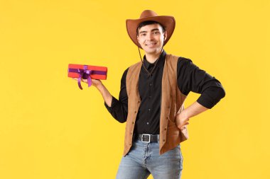 Cadılar Bayramı için kovboy gibi giyinmiş, sarı arka planda hediyeli genç bir adam.