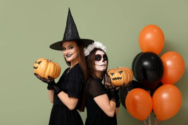 Cadılar Bayramı için giyinmiş genç kadınlar, balkabakları ve balonları yeşil arka planda