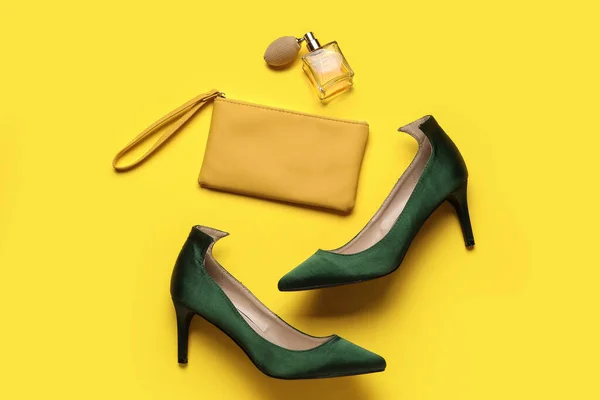 Stylish green high heels with bag and perfume on yellow background