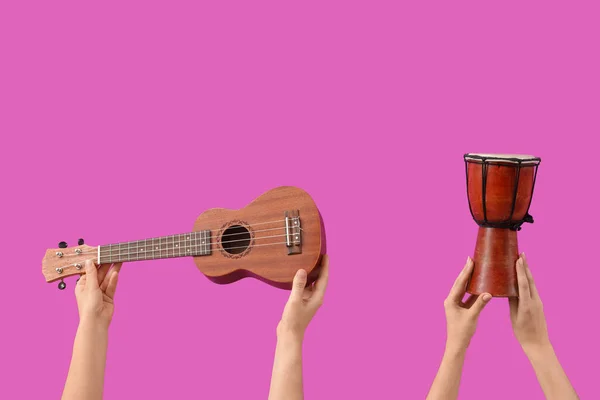Female hands holding ukulele and drum on pink background