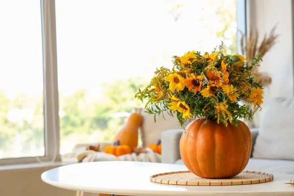 Pumpkin with autumn flowers on table in living room