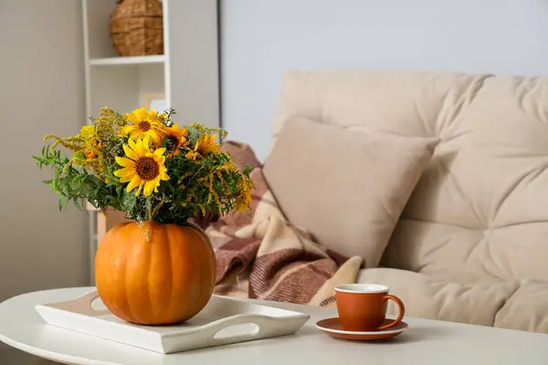 Pumpkin with autumn flowers and cup of coffee on table in living room