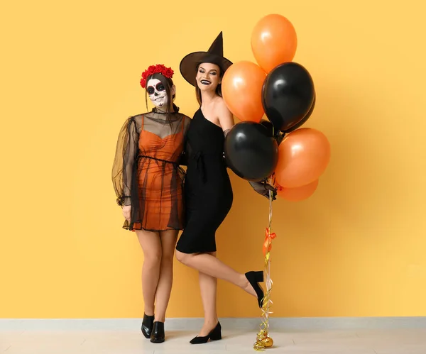 Young women dressed for Halloween with balloons near yellow wall
