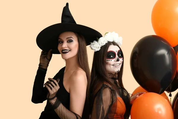 Female friends dressed for Halloween with balloons on beige background