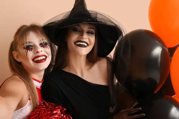 Female friends dressed for Halloween with balloons taking selfie on beige background, closeup