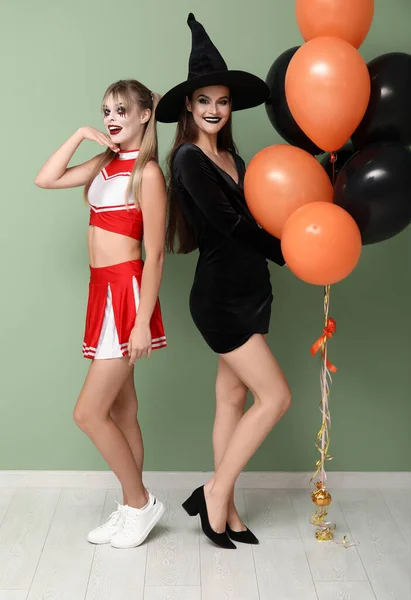 Female friends dressed for Halloween with balloons near green wall
