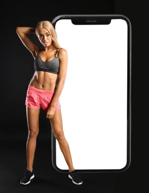 Sportif Afro-Amerikan kadın ve koyu arkaplanda büyük bir akıllı telefon. Kilo verme konsepti