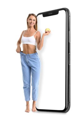 Büyük akıllı telefon ve beyaz arka planda elma tutan bol kotlu güzel genç kadın. Diyet kavramı