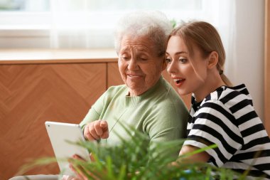 Büyükannesiyle birlikte yatak odasında tablet bilgisayar kullanan genç bir kadın.