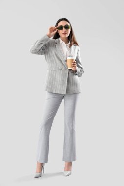 Tarz sahibi takım elbiseli genç bir kadın ve açık arkaplanda bir fincan kahve.