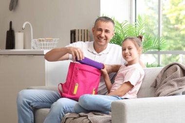 Babası küçük kızına mutfakta okul çantasını toplaması için yardım ediyor.