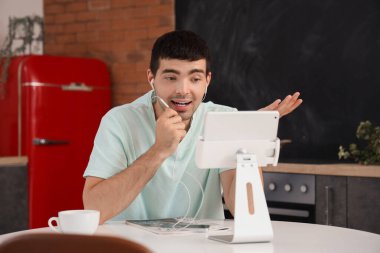 Kulaklıklı genç adam mutfakta video sohbeti yapıyor.