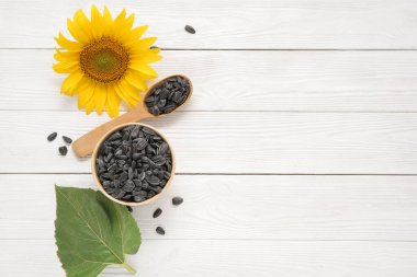 Beyaz ahşap arka planda tohumları olan güzel ayçiçeği ve kase