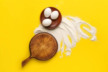 Ahşap kesim tahtası, tavuk yumurtası ve sarı arka planda un kompozisyonu
