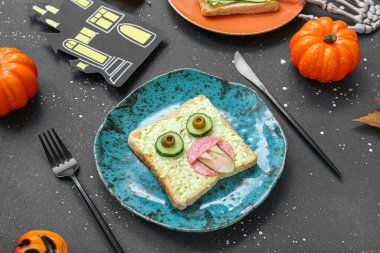 Komik bir Cadılar Bayramı sandviçi tabağı ve koyu arkaplanda süslemeler.