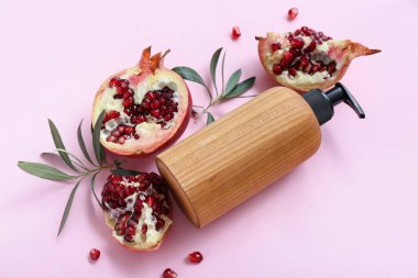 Kozmetik ürün şişesiyle kompozisyon ve pembe arka planda olgun nar.