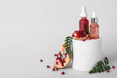 Temel yağ şişeleri, sıva podyum ve hafif arkaplanda nar kompozisyonu