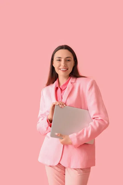ピンクの背景にラップトップとスタイリッシュなスーツの若い女性 — ストック写真