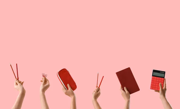 Many hands with school supplies on pink background