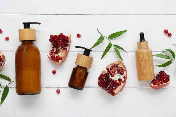 Composition with cosmetic products, pomegranate and plant leaves on light wooden background