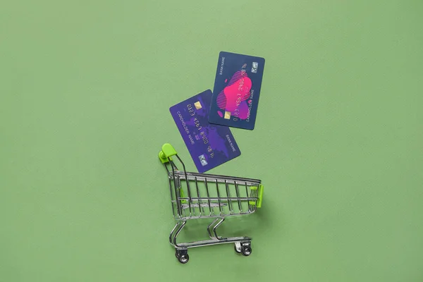 Shopping cart and credit cards on green background