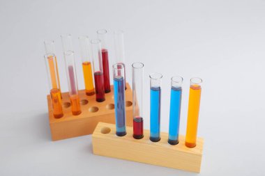 Tahtadan renkli örnekler içeren test tüpleri gri arka planda duruyor.
