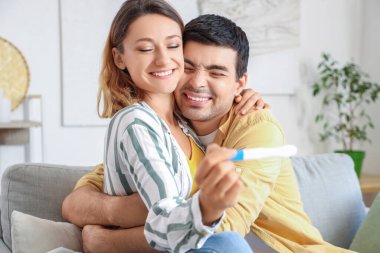 Hamilelik testi olan mutlu genç çift evde sarılıyor.